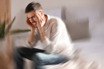 Young man suffering from headache in bedroom