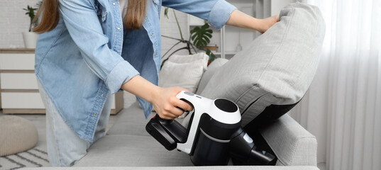 Young woman vacuum cleaning sofa at home © Pixel-Shot