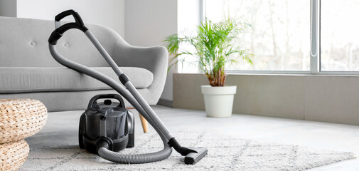 Modern vacuum cleaner near sofa on carpet in living room interior