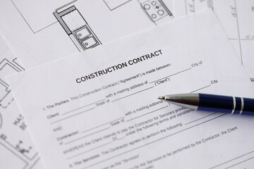 Pen on residential construction agreement and planning blueprints of residential building project