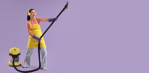 Female janitor with vacuum cleaner listening to music on lilac background with space for text