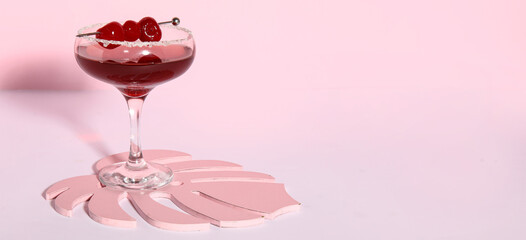 Glass of Cosmopolitan cocktail with cherries on pink background