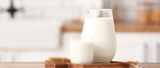 Glass and jug of fresh milk on wooden table
