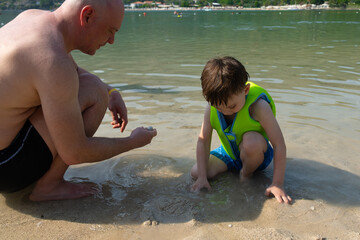 Father and small child spending time together playing on beach in bay during summer vacation