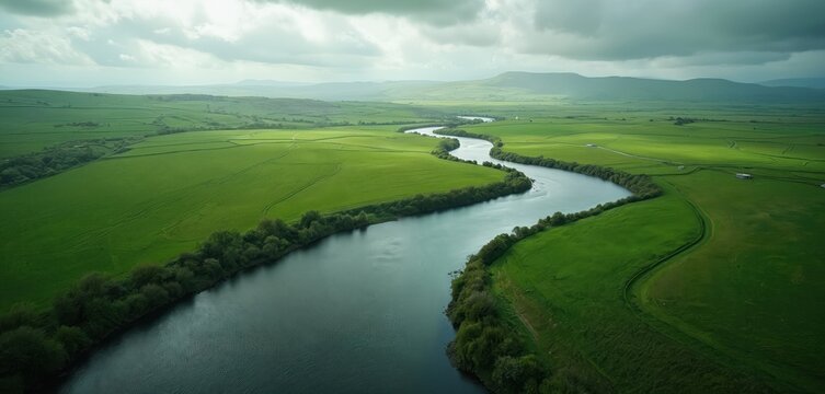 Winding river flows through lush green fields under cloudy sky. Nature landscape evokes tranquility. Beautiful scenic outdoors, perfect for eco travel, relaxation, environmental protection projects.