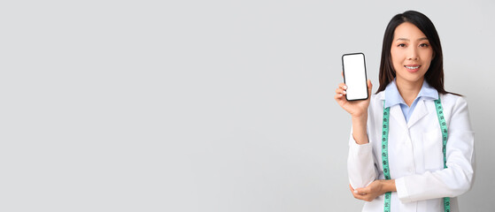 Female Asian nutritionist with mobile phone on light background