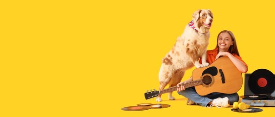 Young woman with guitar and Australian Shepherd dog with vinyl disks and record player on yellow...