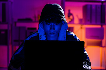 Young Man in Hoodie Working on Laptop in Dark Tech Environment