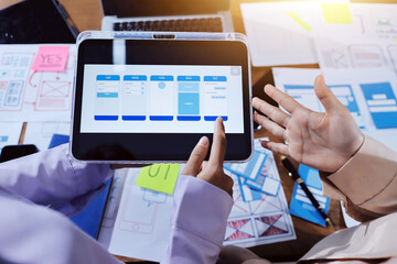 Close up ux developer and ui designer brainstorming about mobile app interface wireframe design on table with customer breif and color code at modern office.Creative digital development agency.