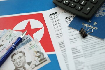 North Korean won money bills lies on table with pen, calculator, passport and tax forms