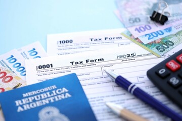 Argentine pesos money bills in big amount lies on table with pen, calculator, passport and tax forms