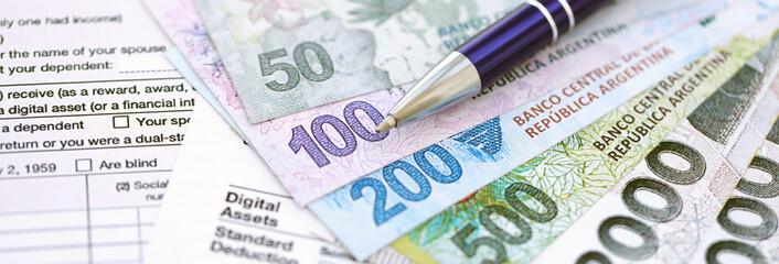 Argentine pesos money bills in big amount lies on table with pen and tax forms close up