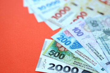 Argentine pesos money bills in big amount lies on red color table close up