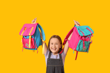 Little girl with backpacks on yellow background