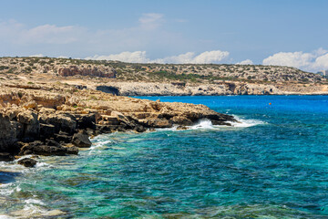 Fototapeta premium Rocky Coastline with Turquoise Water in Cyprus, Scenic view of a rugged rocky shoreline and crystal-clear turquoise sea on a sunny day. summer travel , hot summer 