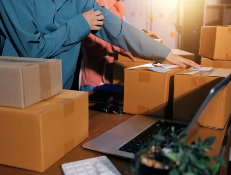 Startup SME small business entrepreneur of freelance Asian woman wearing apron using laptop and box to receive and review orders online to prepare to pack sell to customers, online sme business ideas.