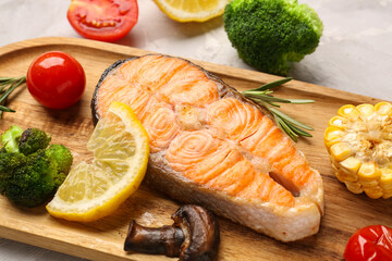Wooden board with tasty grilled salmon steak, lemon and vegetables on table