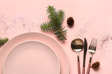 Christmas table setting with fir tree branches, pine cones, plates and cutlery on pink background