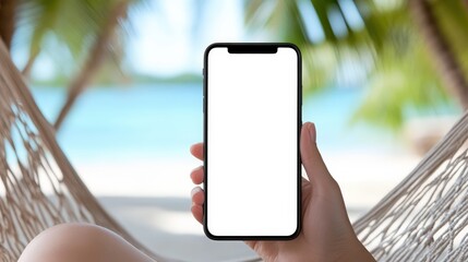 A person holds a smartphone with a blank screen while relaxing in a hammock on a tropical beach with palm trees and clear blue water.