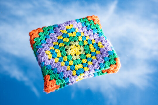 Peque&ntilde;o bolso echo de ganchillo de colores vistosos y alegres sobre un espejo reflejando el cielo con nubes