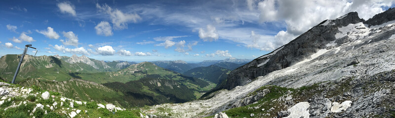 Panoramic mountain landscape with rocky terrain and vibrant greenery under a blue sky