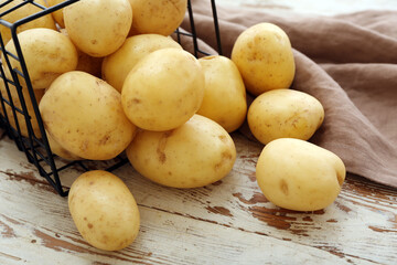 Basket with raw potatoes on white wooden background