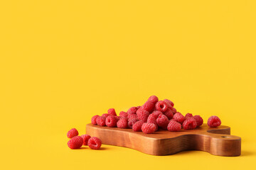 Wooden board with fresh raspberries on yellow background