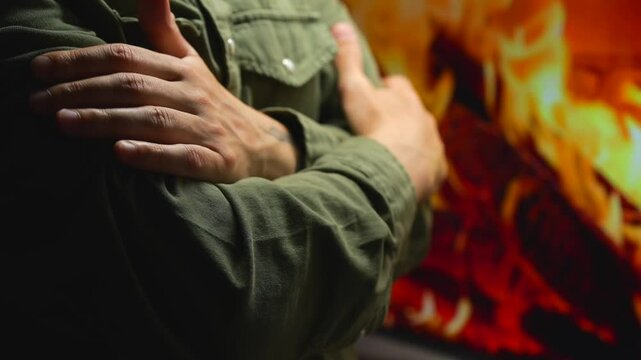 A man in a green shirt warms himself by the fireplace in his room in winter.
A man stands by the fireplace and hugs himself with his hands to warm himself by the fireplace burning in the house