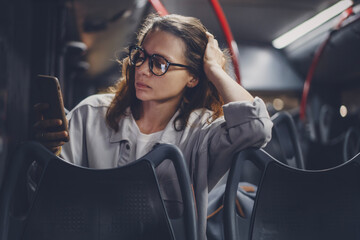 Young cute woman using mobile phone in night city bus