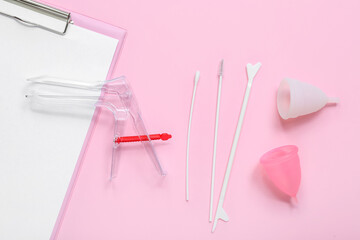 Clipboard with gynecological speculum, menstrual cups and pap smear test tools on pink background