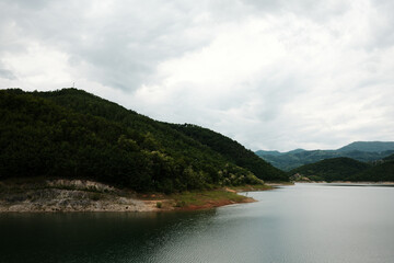 Curving shoreline and forested slopes of Rovni Lake near Valjevo, Serbia, on a cloudy spring day
