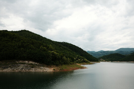 Curving shoreline and forested slopes of Rovni Lake near Valjevo, Serbia, on a cloudy spring day