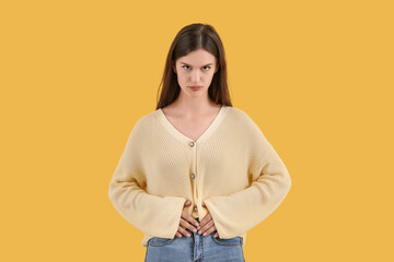 Young woman suffering from stomach ache on yellow background