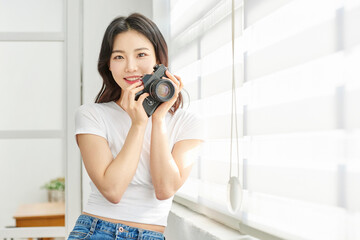 Young Asian Woman Photographer in White T-Shirt Holding Vintage Camera by Bright Window Indoors