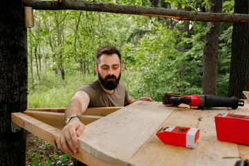brutal young brunette man, dad with beard is nailing building a tree house to his little son with...