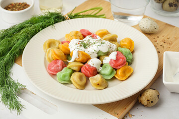 Plate of boiled colorful dumplings with sour cream on white background