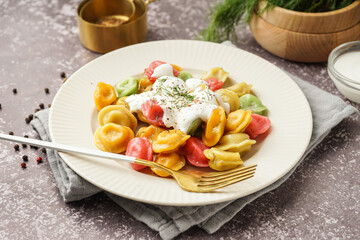 Plate of boiled colorful dumplings with sour cream and dill on dark background