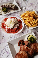 Overhead view of a complete Balkan meal: grilled meat, fresh tomato salad with cheese, and crinkle fries in a Serbian restaurant
