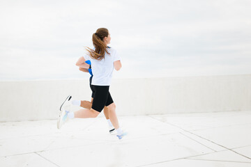 Running on a rooftop in a cityscape, young athlete enjoys exercise under a cloudy sky during...