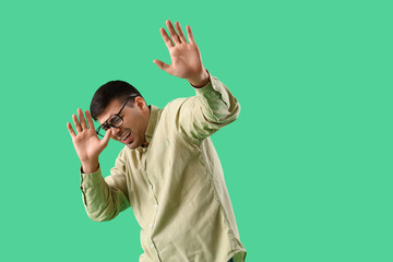 Afraid young man in eyeglasses on green background
