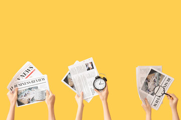 Hands holding alarm clock, newspapers, cup and magnifier on yellow background
