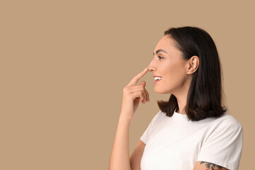 Young woman touching her nose on beige background