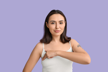 Young woman checking her breast on lilac background. Cancer awareness concept