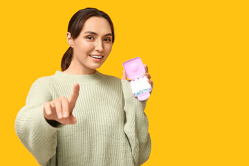 Beautiful young woman with tampons storage box pointing at viewer on yellow background