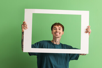 Happy young man holding white photo frame on green background