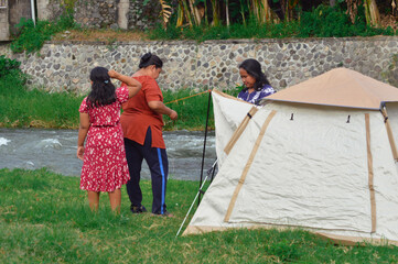 Two mothers pull and secure the canopy ropes while the young girl looks around curiously,...