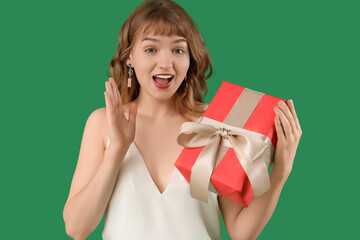 Beautiful young shocked woman with gift box on green background