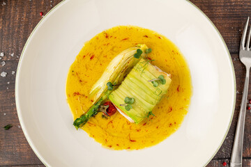 Zucchini-wrapped fish fillet in saffron-infused yellow sauce