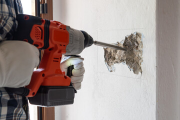 Carpenter electrician with demolition hammer prepares the cavity in the wall where to insert the built-in electrical panel. Work safely with protective gloves. Construction industry.