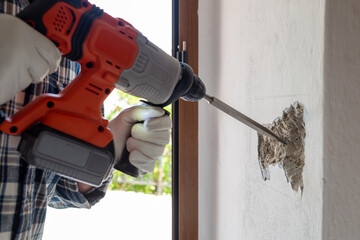 Carpenter electrician with demolition hammer prepares the cavity in the wall where to insert the...